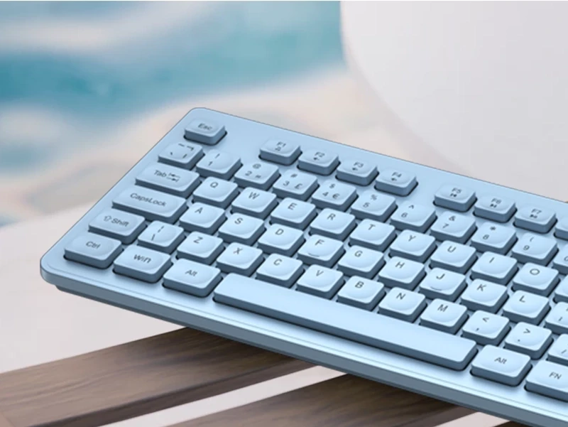 Na obrazie widoczna jest niebieska klawiatura z układem QWERTY, umieszczona na drewnianej powierzchni. W tle znajduje się rozmyte, jasne tło.