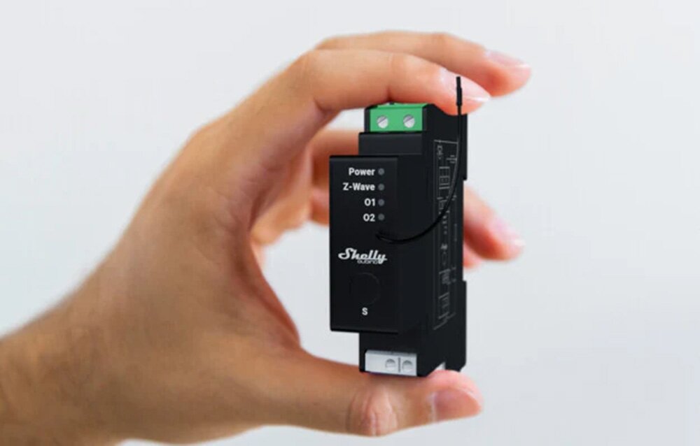 Przekaźnik SHELLY Wave Pro Shutter, sterowanie, napęd, silnik, montaż, na szarym tle dłoń trzyma przekaźnik frontem prawo skos