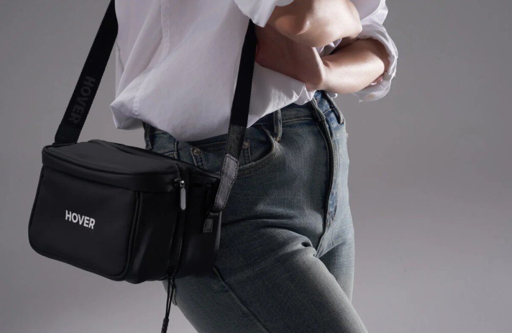 Torba HOVERAIR Multi-functional Carry Bag Osoba w białej koszuli i dżinsach z przewieszoną przez ramię czarną torbą z logo 'HOVER', opis