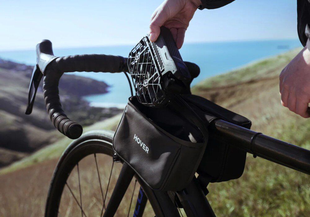 Torba HOVERAIR Multi-functional Carry Bag Rowerzysta wkładający drona do torby zamocowanej na ramie roweru na tle morza, przeznaczenie, zastosowanie