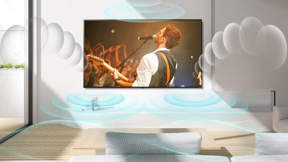 W nowoczesnym salonie na ścianie wisi duży telewizor, na którym wyświetlany jest koncert muzyczny. Wokół telewizora widoczne są graficzne efekty dźwiękowe, sugerujące przestrzenny dźwięk.
