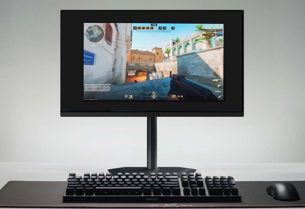 Monitor GIGABYTE MO27Q2 Monitor na biurku z wyświetlonym obrazem gry w trybie 24-calowym, z widoczną klawiaturą i myszką, funkcje dla graczy