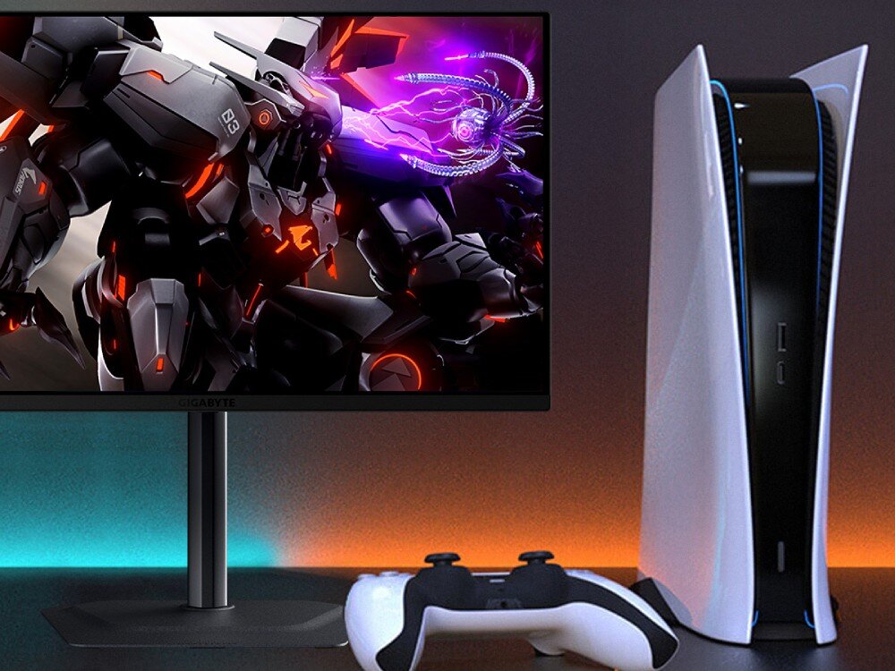 Monitor GIGABYTE MO27Q2 Monitor obok konsoli do gier i kontrolera, na ekranie dynamiczna scena z postacią mecha, kompatybilność z konsolami