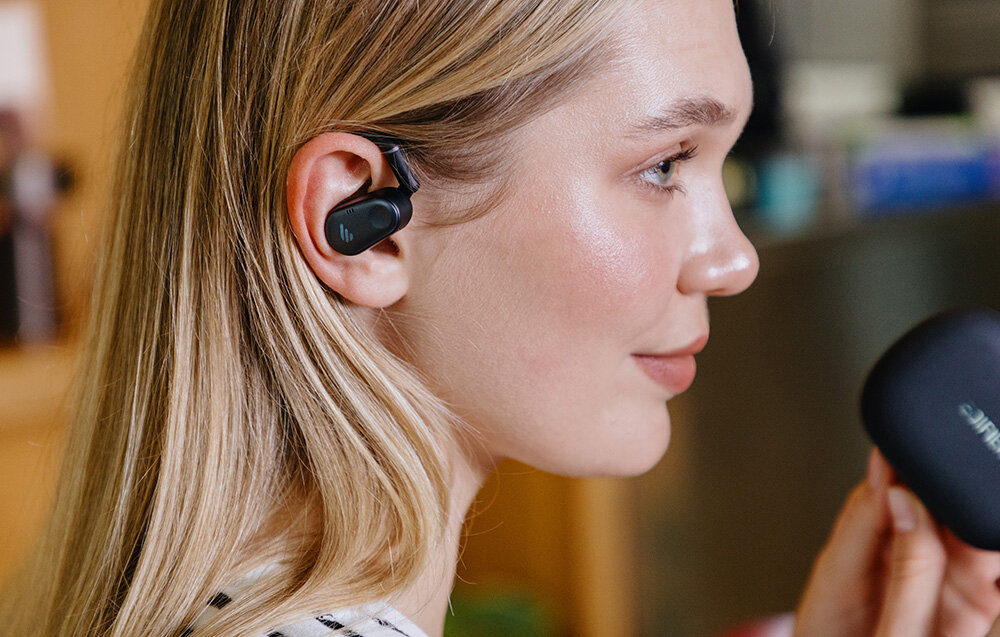 Słuchawki EDIFIER Comfo Flex komfort otwarta konstrukcja ergonomia, osoba z założonymi słuchawkami trzymająca w rękach etui ładujące