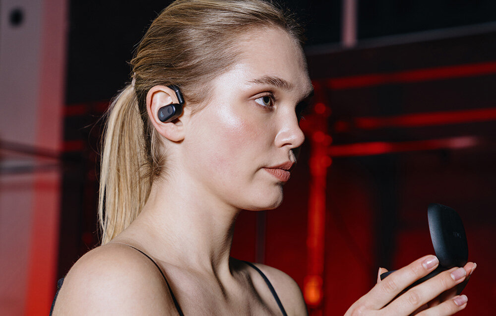 Słuchawki EDIFIER Comfo Flex bluetooth multipoint stabilne połączenie, osoba z założonymi słuchawkami trzymająca w rękach etui ładujące