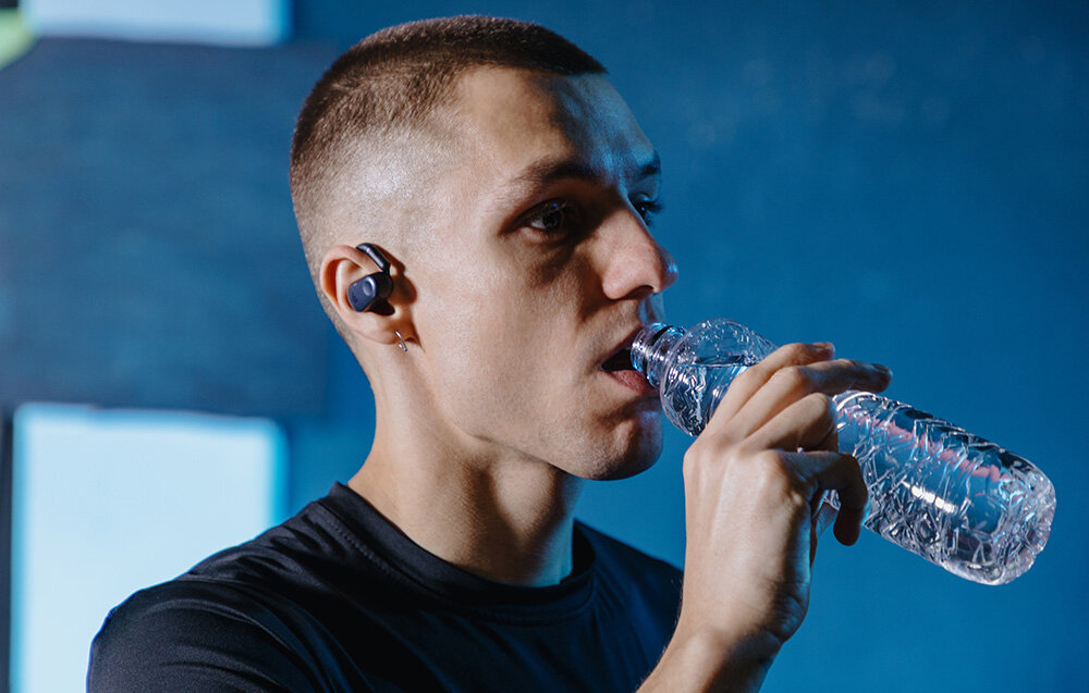 Słuchawki EDIFIER Comfo Flex tryby dźwięku muzyka gry filmy, osoba z założonymi słuchawkami trzymająca w ręku butelkę wody