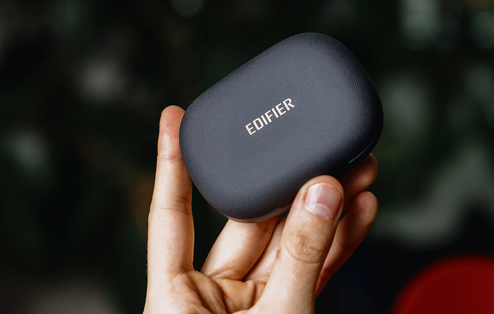 Słuchawki EDIFIER Comfo Flex długi czas pracy szybkie ładowanie IP55, ręka trzymająca etui ładujące na ciemnym tle