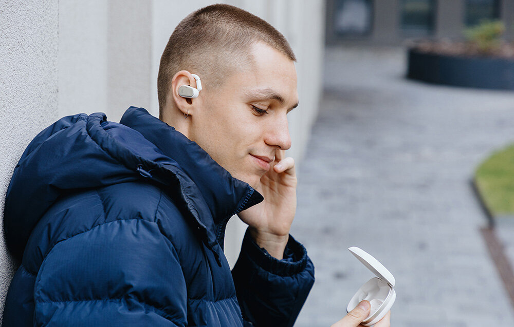Słuchawki EDIFIER Comfo Flex komfort otwarta konstrukcja ergonomia, osoba z założonymi słuchawkami trzymająca w ręku etui ładujące
