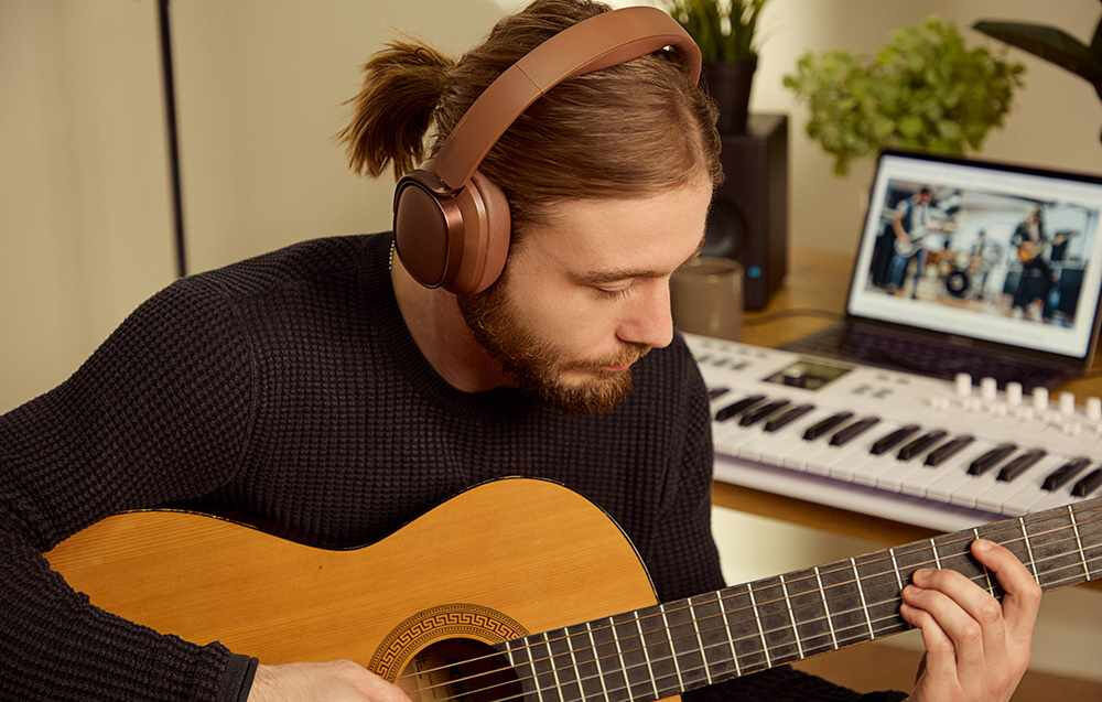 EDIFIER ES850NB ANC słuchawki Hi-Res Audio 40 mm tytanowa membrana LDAC SBC Bluetooth, osoba z założonymi słuchawkami nausznymi trzymająca gitarę w rękach