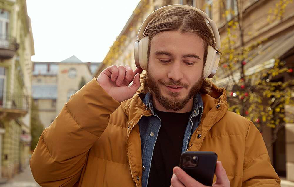 EDIFIER ES850NB ANC słuchawki bezprzewodowe czas pracy 92 godziny szybkie ładowanie 11,5h po 15 minutach, osoba z założonymi słuchawkami nausznymi trzymająca w ręku smartfona