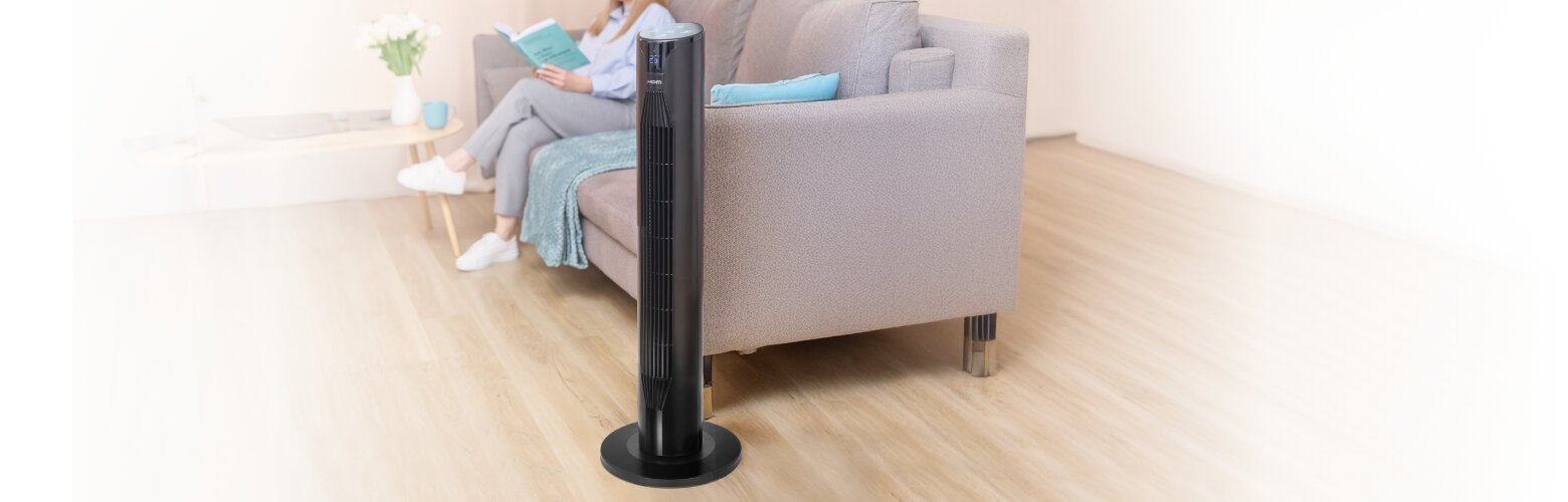 Wentylator kolumnowy MWP-26/C stoi obok kanapy. W tle na kanapie kobieta czyta książkę.