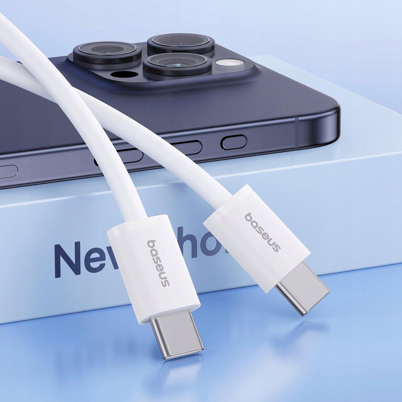 Na obrazie widoczny jest biały kabel USB C z logo \'baseus\' na tle pudełka z napisem \'New phone\' oraz fragmentem telefonu z trzema obiektywami aparatu.