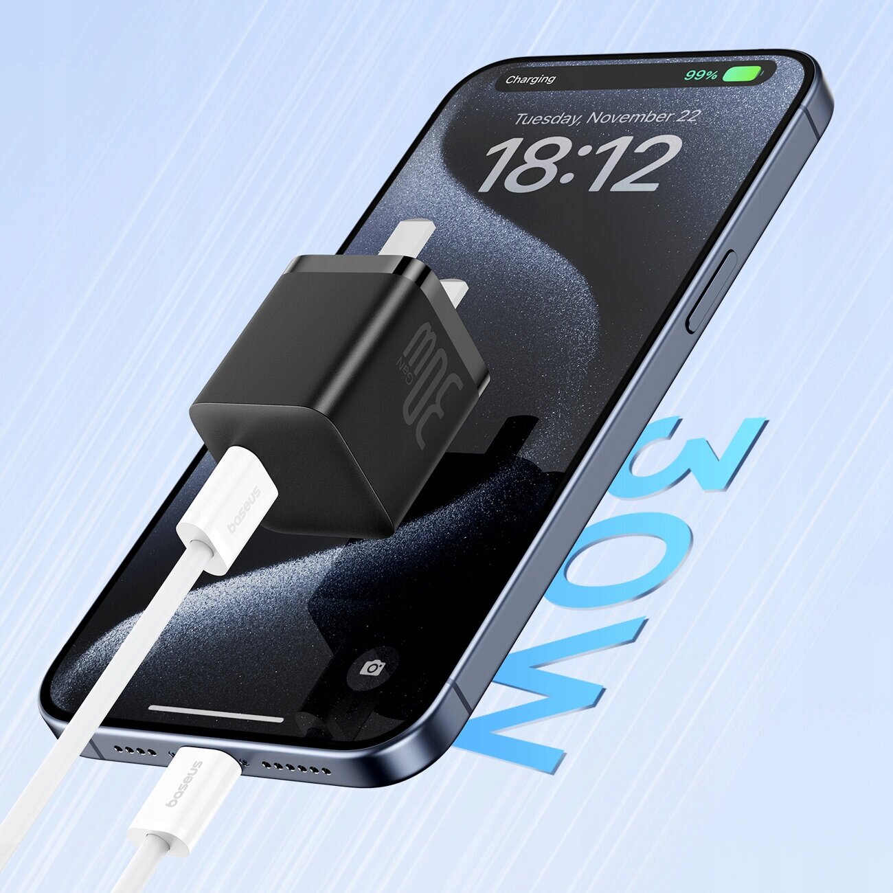 Na obrazie widać smartfon z wyświetlaczem pokazującym godzinę 18:12 i datę Tuesday, November 22, z podłączonym kablem USB C oraz czarną ładowarką z napisem \'30W\'. Na ekranie telefonu widoczny jest wskaźnik naładowania baterii na poziomie 99% oraz napis \'Charging\'.
