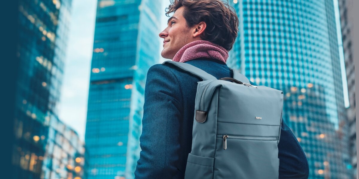 Plecak na laptopa HAMA Ultimate 16.2 cali Niebieski Mężczyzna w garniturze niosący niebieski, elegancki plecak na laptopa Hama na tle nowoczesnych wieżowców.