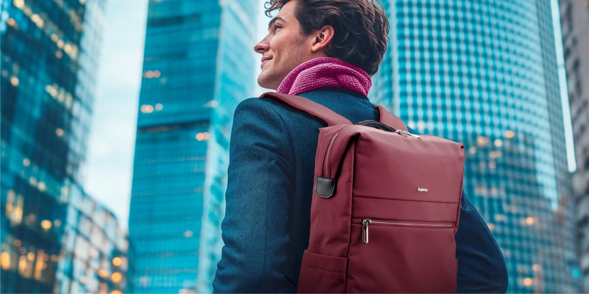 Plecak na laptopa HAMA Ultimate 16.2 cali Czerwony Mężczyzna w garniturze niosący elegancki plecak na laptopa Hama na tle nowoczesnych wieżowców.
