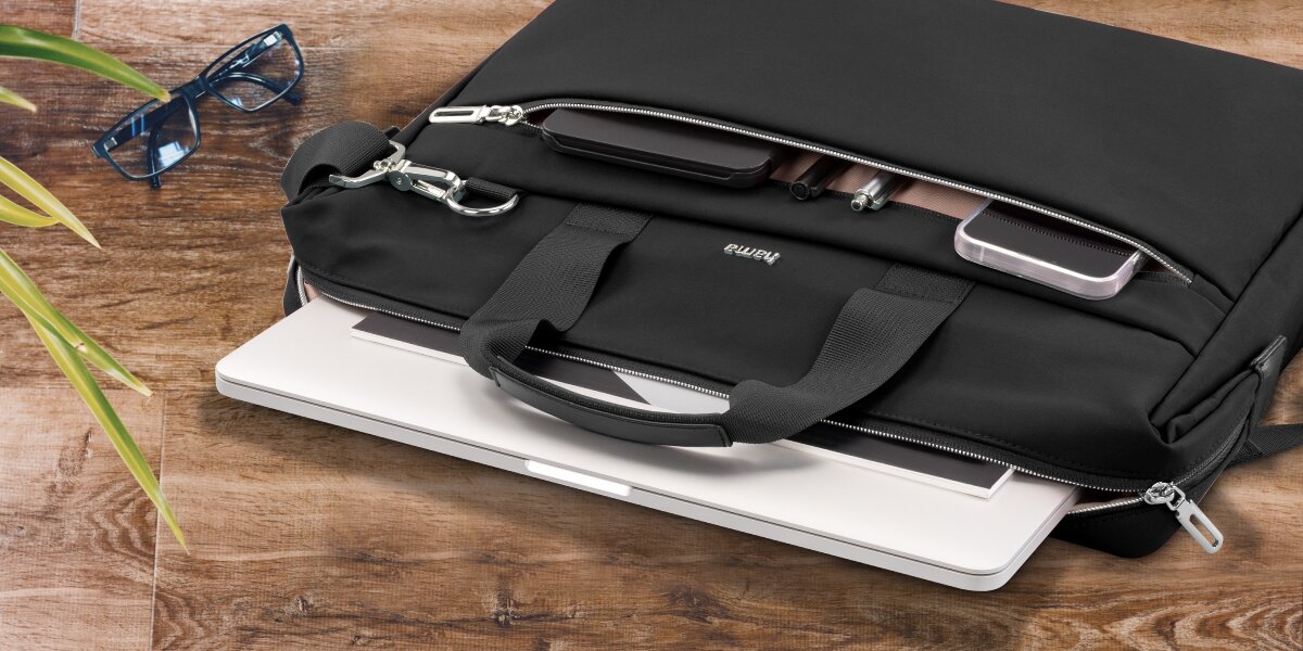 Torba na laptopa HAMA Ultimate 15.6 - 16.2 cala Czarny Torba na laptopa Hama leżąca na drewnianym blacie z otwartą przegrodą, z której wysunięty jest biały laptop.