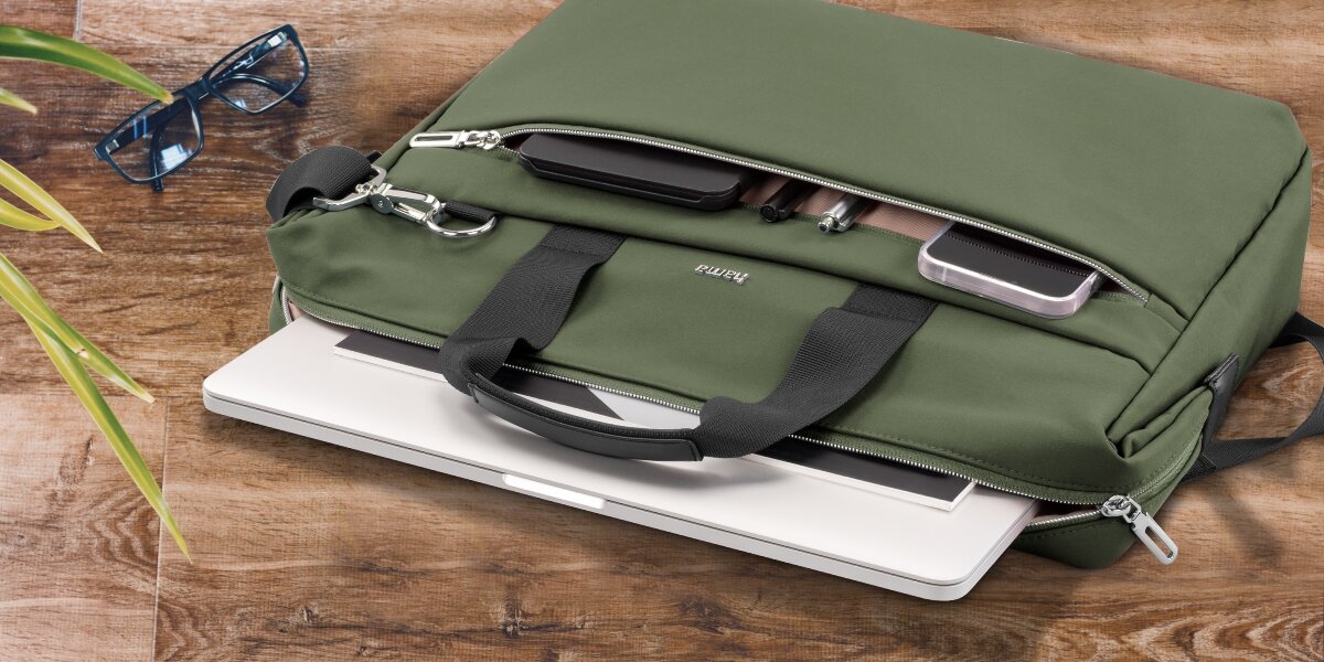 Torba na laptopa HAMA Ultimate 15.6 - 16.2 cala Zielony Torba na laptopa Hama leżąca na drewnianym blacie z otwartą przegrodą, z której wysunięty jest biały laptop.