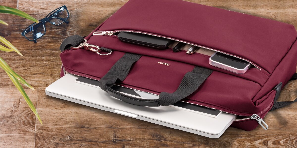 Torba na laptopa HAMA Ultimate 15.6 - 16.2 cala Czerwony Torba na laptopa Hama leżąca na drewnianym blacie z otwartą przegrodą, z której wysunięty jest biały laptop.