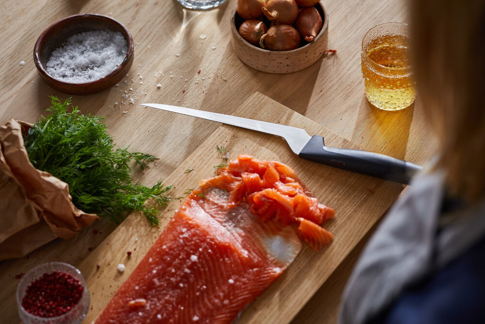 Nóż FISKARS Hard Edge 1054946 ryba leży na desce obok położony jest nóż z czarną rączką Ostrze z wysokiej jakości japońskiej stali nierdzewnej precyzja efektywność trwałość dynamiczne cięcie z dużą siłą subtelna precyzja w codziennym gotowaniu przy wymagających technikach kulinarnych