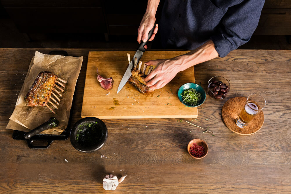 Nóż FISKARS Hard Edge 1051760 osoba kroi mięso na desce nożem z czarną rączką Ostrze z wysokiej jakości japońskiej stali nierdzewnej precyzja efektywność trwałość dynamiczne cięcie z dużą siłą subtelna precyzja w codziennym gotowaniu przy wymagających technikach kulinarnych