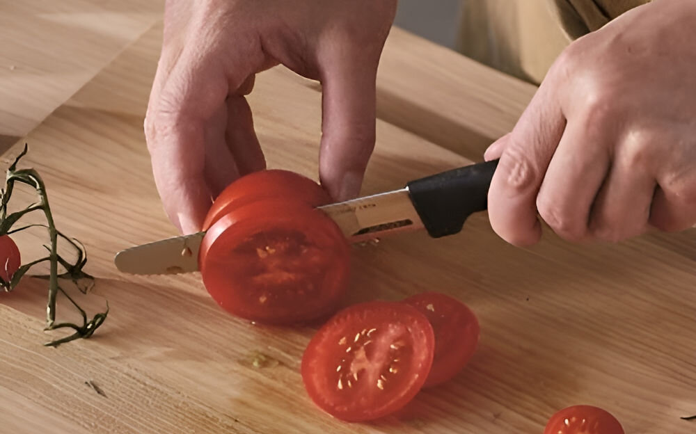 Nóż FISKARS Hard Edge 1054947 osoba kroi pomidory na desce nożem z czarną rączką Ostrze o długości 11,4 cm całkowitej długości 23,4 cm krojenie waży jedynie 55 g