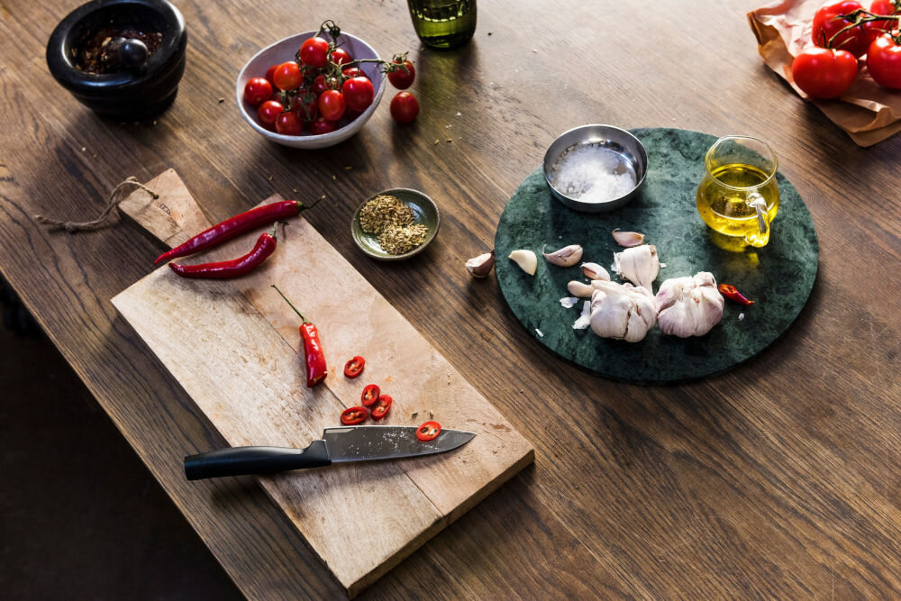 Nóż FISKARS Hard Edge 1051749 deska na desce znajduje się nóż z czarną rękojeścią obok leżą pokrojone warzywa dla każdego Ostrze o długości 13,5 cm całkowitej długości 25,1 cm krojenie siekanie waży jedynie 66 g