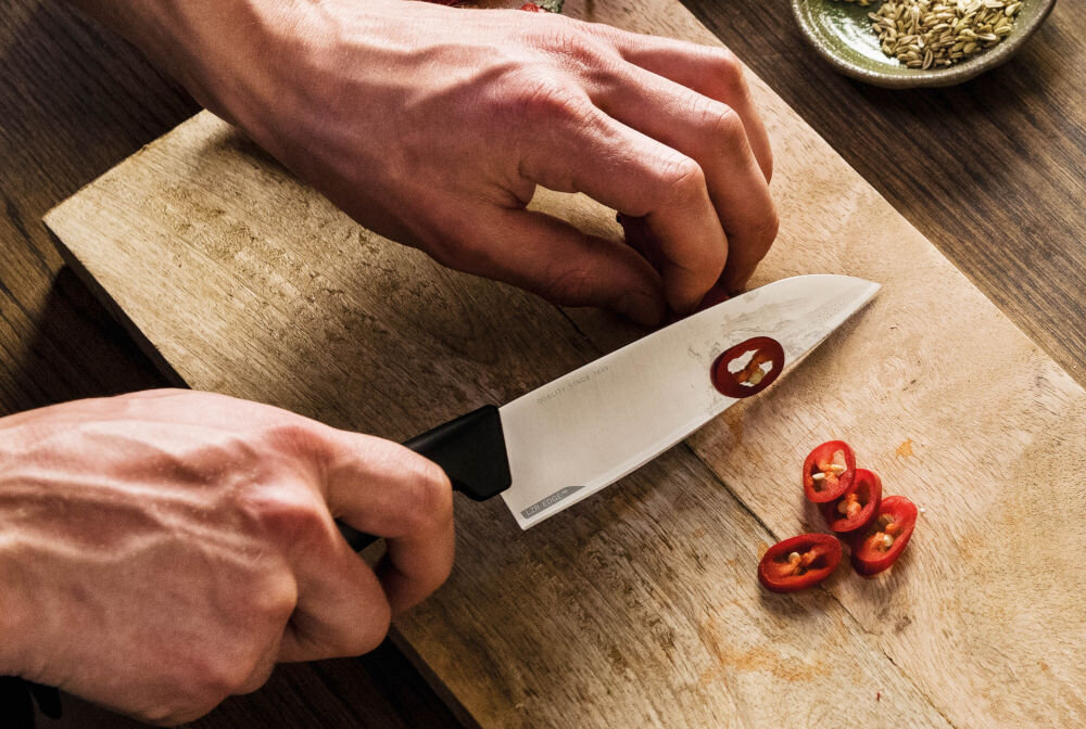 Nóż FISKARS Hard Edge 1051749 osoba kroi papryczkę na desce nożem z czarną rączką Ostrze z wysokiej jakości japońskiej stali nierdzewnej precyzja efektywność trwałość dynamiczne cięcie z dużą siłą subtelna precyzja w codziennym gotowaniu przy wymagających technikach kulinarnych