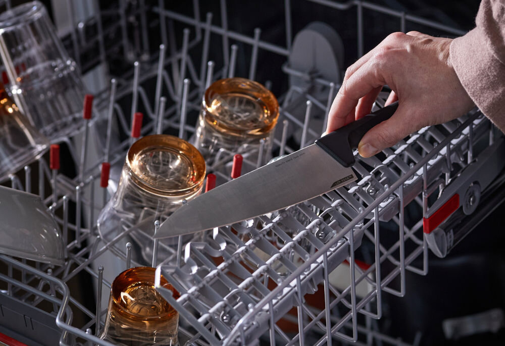 Nóż FISKARS Hard Edge 1051762 osoba wkłada nóż z czarną rączką do zmywarki design funkcjonalność rękojeść ergonomicznie wyprofilowana wzbogacona o strukturę 3D pewny wygodny chwyt osłona na palce Stworzony w Finlandii z troską o środowisko ekologicznym opakowaniem z kartonu o minimalnej zawartości plastiku można myć w zmywarce