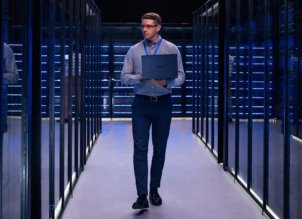 Komputer ASUS ExpertCenter D501MER-514500152X Mężczyzna idący przez korytarz serwerowni trzymający zamknięty laptop w dłoniach, zarządzanie, kontrola