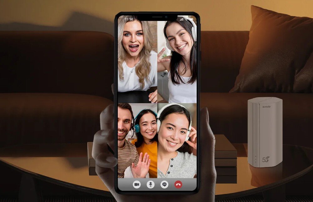 Router TENDA 5G01 Osoba trzymająca smartfon podczas rozmowy wideo z kilkoma osobami. W tle pomieszczenie z sofą, stolikiem i widocznym białym urządzeniem sieciowym, prędkość, łączność 5G