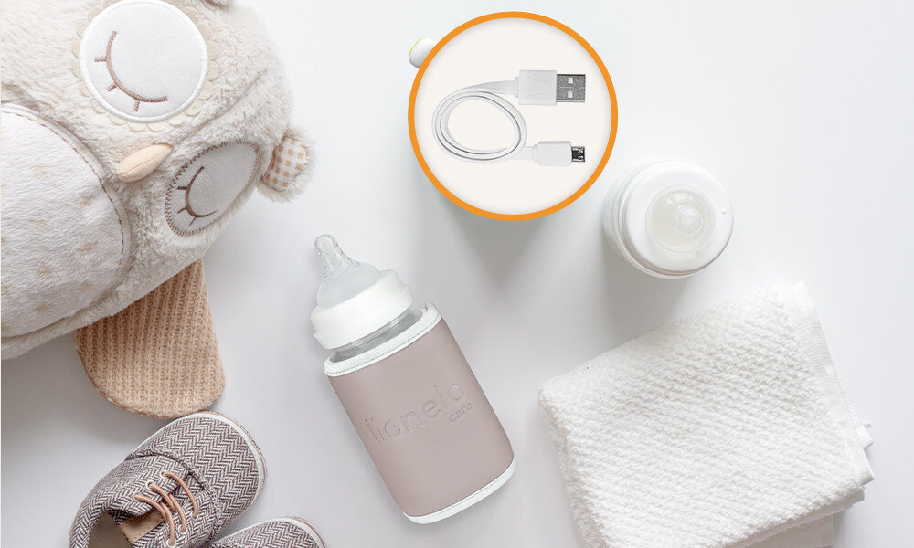 Na zdjęciu znajduje się butelka z napisem \'Lionelo care\', kabel USB oraz pluszowa zabawka w kształcie sowy. Obok leży para dziecięcych butów i biała tkanina.