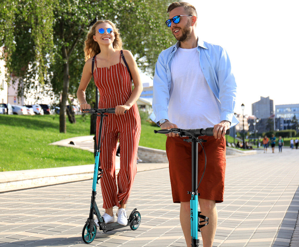 Hulajnoga NILS EXTREME HM124T Turkusowy miasto park droga dwie osoby jadą na hulajnogach po chodniku w dali widać ludzi budynki drzewa niebo możliwość regulacji wysokości kierownicy w zakresie od 93 do 110 cm komfort jazdy i kontrolę nad pojazdem płynne prowadzenie hulajnogi wygoda oraz bezpieczeństwo składane uchwyty antypoślizgowy materiał TPR