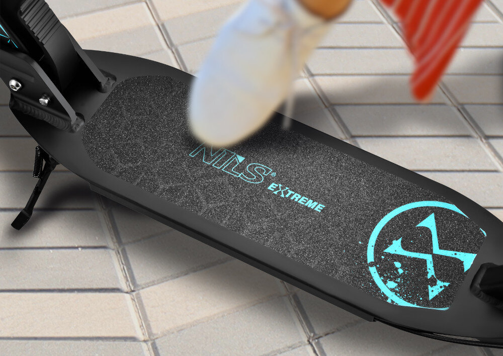 Hulajnoga NILS EXTREME HM124T Turkusowy chodnik zbliżenie na deck osoba dotyka stopą decku deck wykonany z aluminium  antypoślizgowy materiał minimalizują ryzyko poślizgnięcia się stopy szeroki deck kontrola nad hulajnogą ułatwia wykonywanie skrętów stabilna platforma