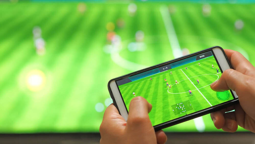 Odtwarzacz multimedialny 4K TESLA MediaBox XG500 Android TV dostęp do aplikacji na dużym ekranie, ekran telewizora w tle, ręce trzymające smartfona