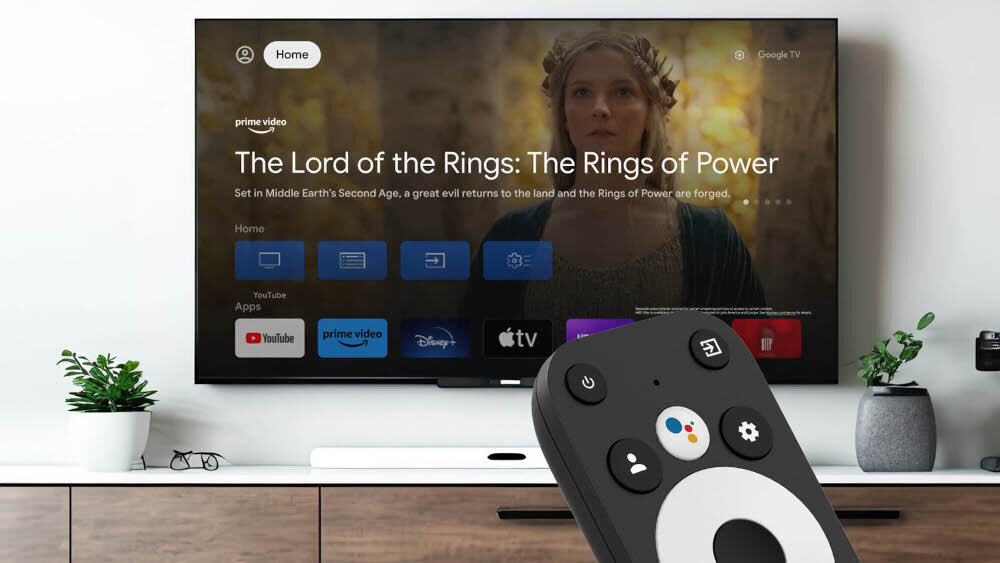 Odtwarzacz multimedialny 4K TESLA MediaBox XG500 z aplikacjami YouTube Netflix Spotify, pilot na pierwszym planie, telewizor zawieszony na ścianie nad komodą