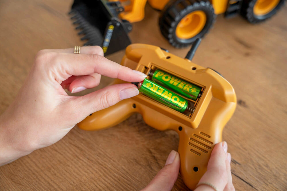 ŁADOWARKA RC S-LINE RCC204 Zabawkowa ładowarka kołowa na drewnianej podłodze w jasnym pokoju dziecięcym z jasnoniebieskimi ścianami ozdobionymi kolorowymi kółkami i proporczykami. W tle widoczny jest biały regał z licznymi książkami i półkami na zabawki.