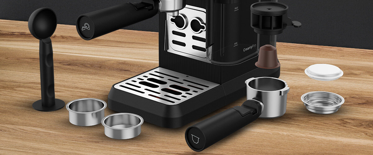 Na drewnianym blacie znajduje się ekspres do kawy z metalową tacką ociekową oraz różne akcesoria, takie jak uchwyty i sitka. Na ekspresie widoczny jest napis \'CaffeExperto\'.