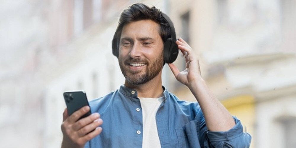 Słuchawki nauszne HYUNDAI HBTM45B Bluetooth kabel AUX 3.5 mm tryb przewodowy, osoba z założonymi słuchawkami nausznymi oraz smartfonem w ręku