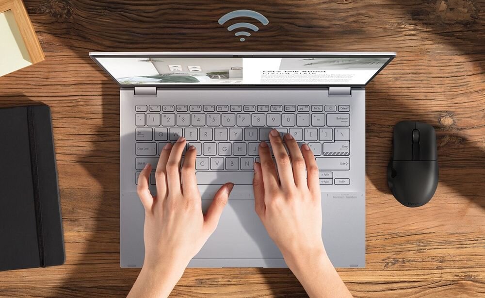 ASUS VivoBook S 14 Flip w widoku z góry z rękoma na klawiaturze na drewnianym biurku z symbolem WiFi, prezentującym łączność WiFi 6E z dostępem do pasma 6GHz, prędkościami do 2.4Gbps i obsługą 7 dodatkowych kanałów 160MHz dla maksymalnej wydajności - WiFi 6E