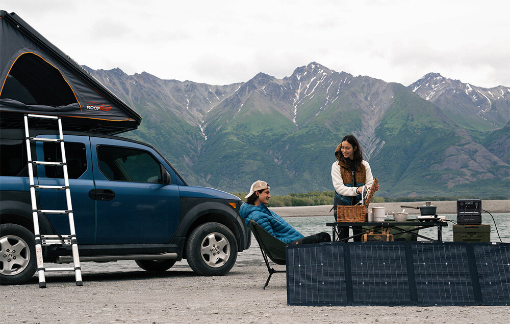 Stacja zasilania ECOFLOW River 3 Max 572 Wh Bank energii, Pojemna i mobilna forma, Para odpoczywa przy campingowym aucie, w tle góry, stacja podłączona do sprzętu biwakowego