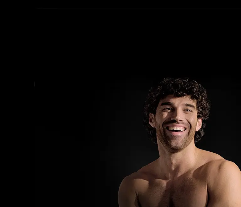 Portret uśmiechniętego mężczyzny z ciemnymi, kręconymi włosami.