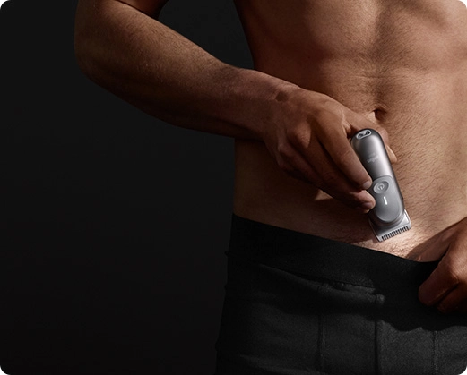 Mężczyzna golący okolice brzucha srebrną maszynką do ciała Braun.