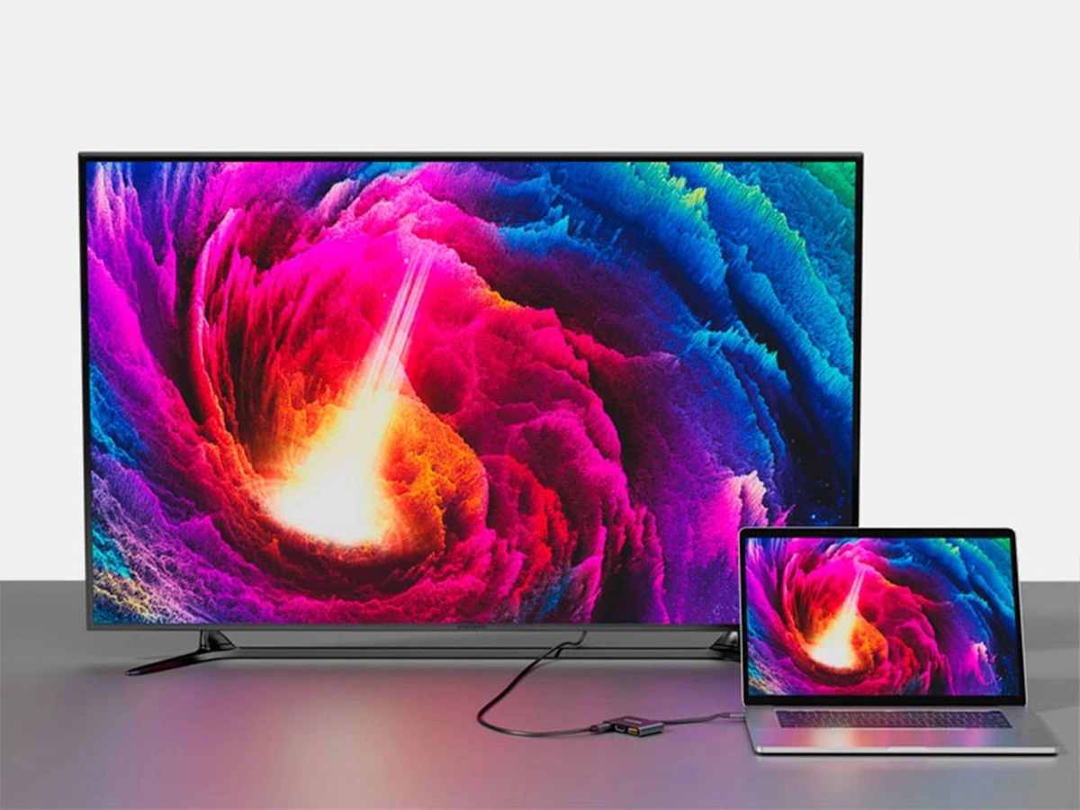 Na obrazie widać duży monitor i laptop, oba wyświetlają ten sam kolorowy, abstrakcyjny wzór. Urządzenia są połączone za pomocą szarego huba USB-C.