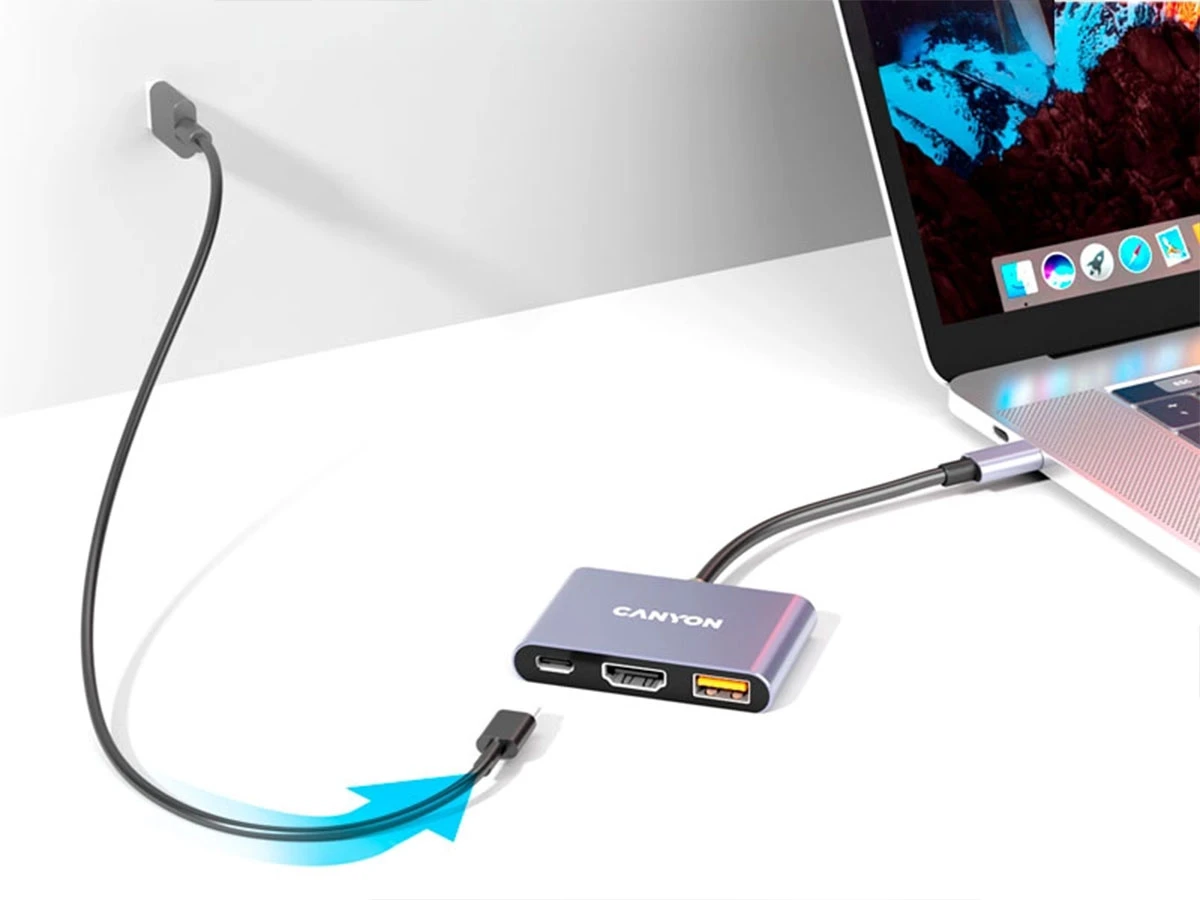 Na obrazie widoczny jest szary hub USB-C z trzema portami, podłączony do laptopa. Na hubie znajduje się logo \'CANYON\'.