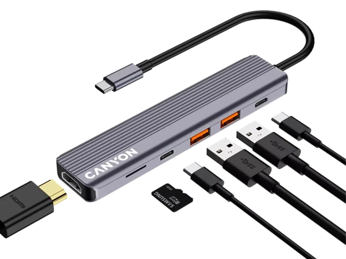 Szary hub USB-C z logo \'CANYON\', posiada kilka portów, w tym HDMI, USB i czytnik kart. Obok znajdują się różne kable i adaptery, w tym USB i HDMI.
