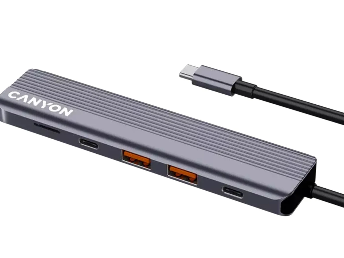 Szary hub USB-C z logo \'CANYON\' posiada kilka portów, w tym USB i czytnik kart. Do urządzenia podłączony jest czarny kabel USB-C.