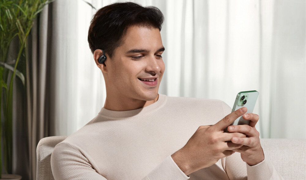 Słuchawki powietrzne SOUNDCORE AeroFit 2 Bluetooth 5.4 multi-point stabilne połączenie, osoba trzymająca telefon w rękach z założonymi słuchawkami
