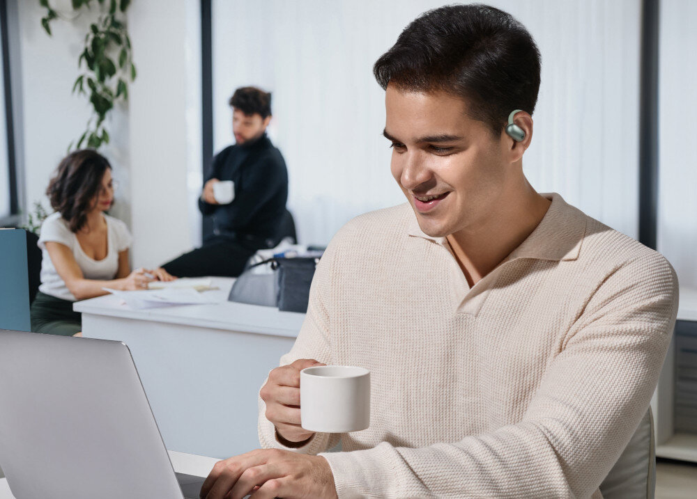 Słuchawki powietrzne SOUNDCORE AeroFit 2 otwarta konstrukcja zaczepy wentylacja higiena, osoba siedząca przy laptopie z założonymi słuchawkami