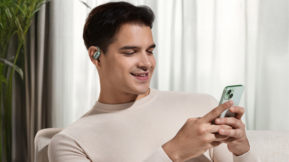 Słuchawki powietrzne SOUNDCORE AeroFit 2 Bluetooth 5.4 multi-point stabilne połączenie, osoba trzymająca telefon w rękach z założonymi słuchawkami