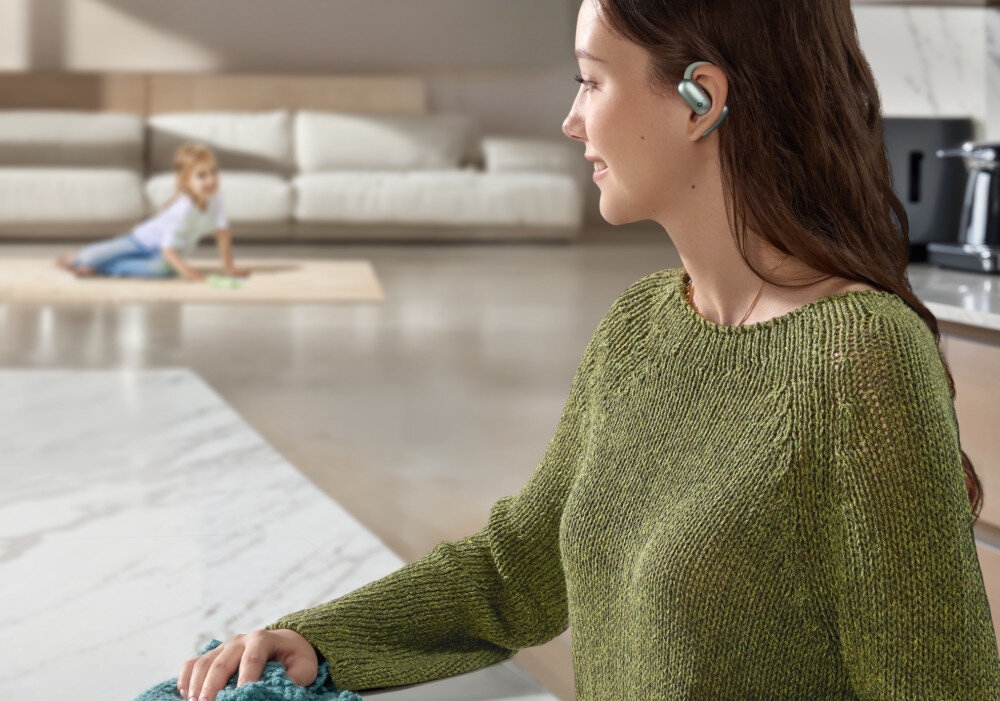 Słuchawki powietrzne SOUNDCORE AeroFit 2 sterowanie dotykowe asystent głosowy wygoda obsługi, osoba stojąca przy blacie z założonymi słuchawkami